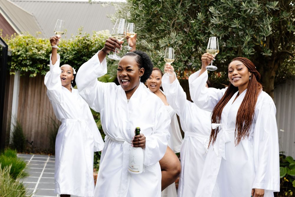 A group of people wearing white clothing dance and celebrate together in an outdoor setting.