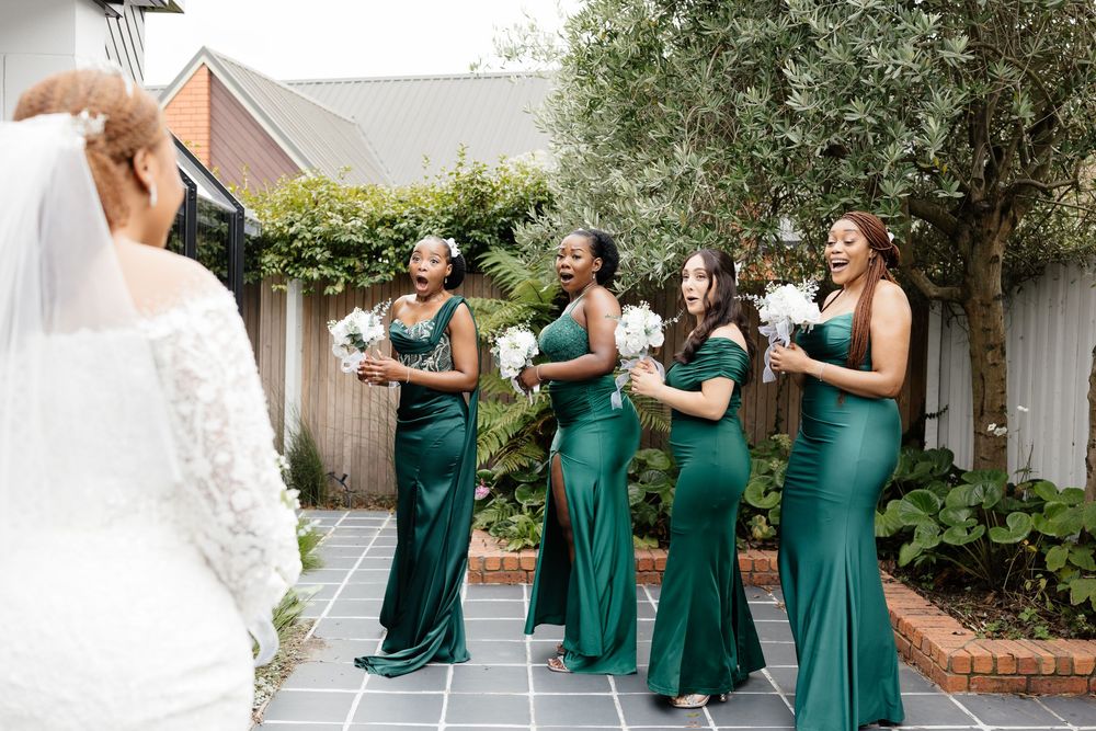 Bridesmaids in emerald green dresses share a joyful moment during a wedding photo session.