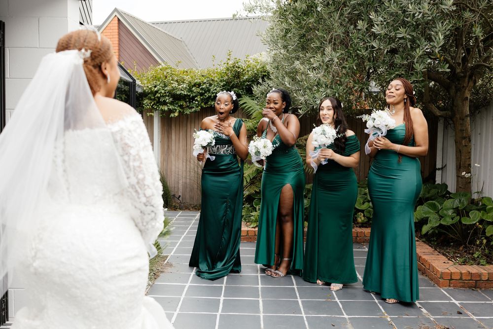 Wedding party members in emerald green dresses pose together during outdoor celebration.