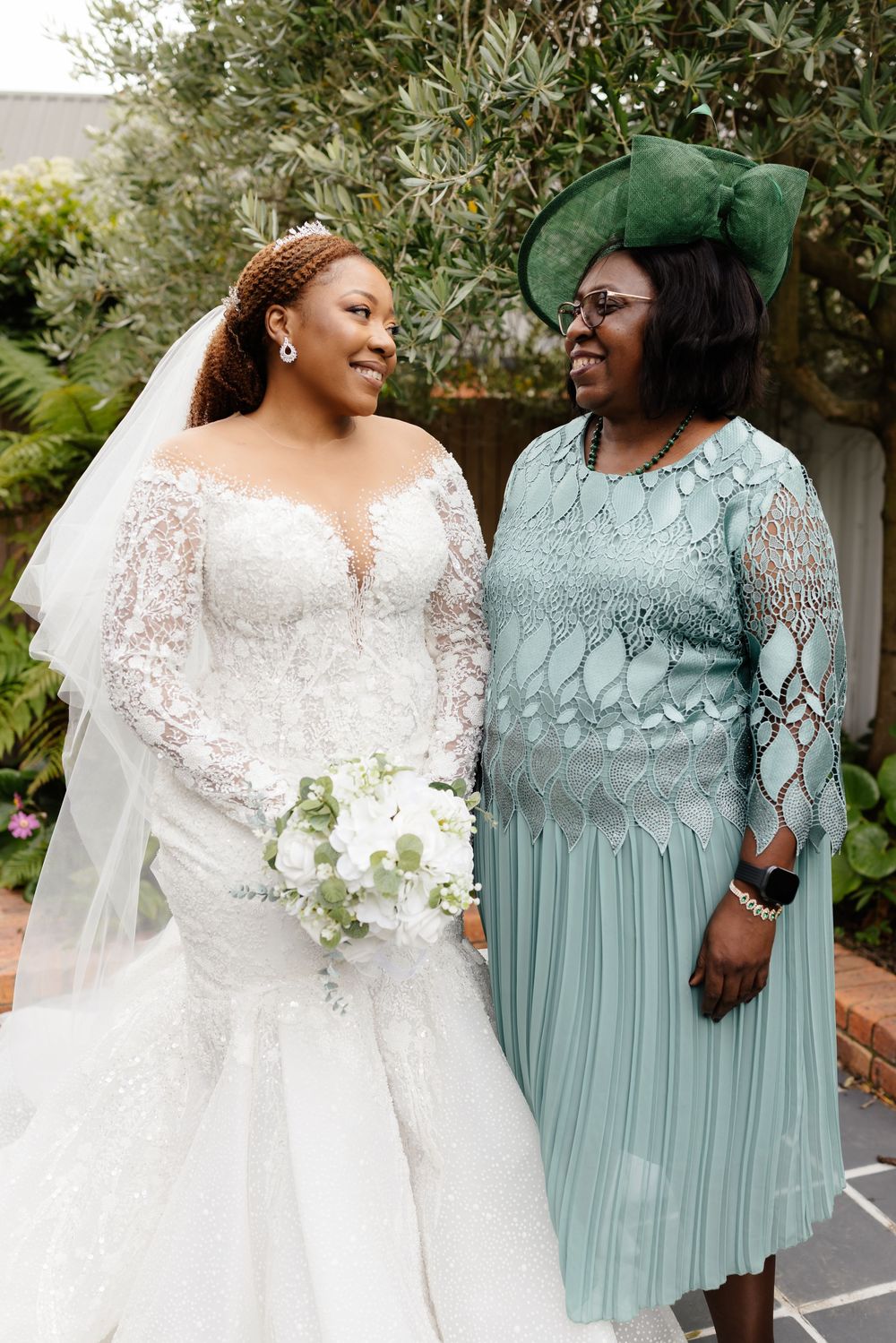 Wedding party wearing white lace and mint green dresses posing outdoors with bouquets.