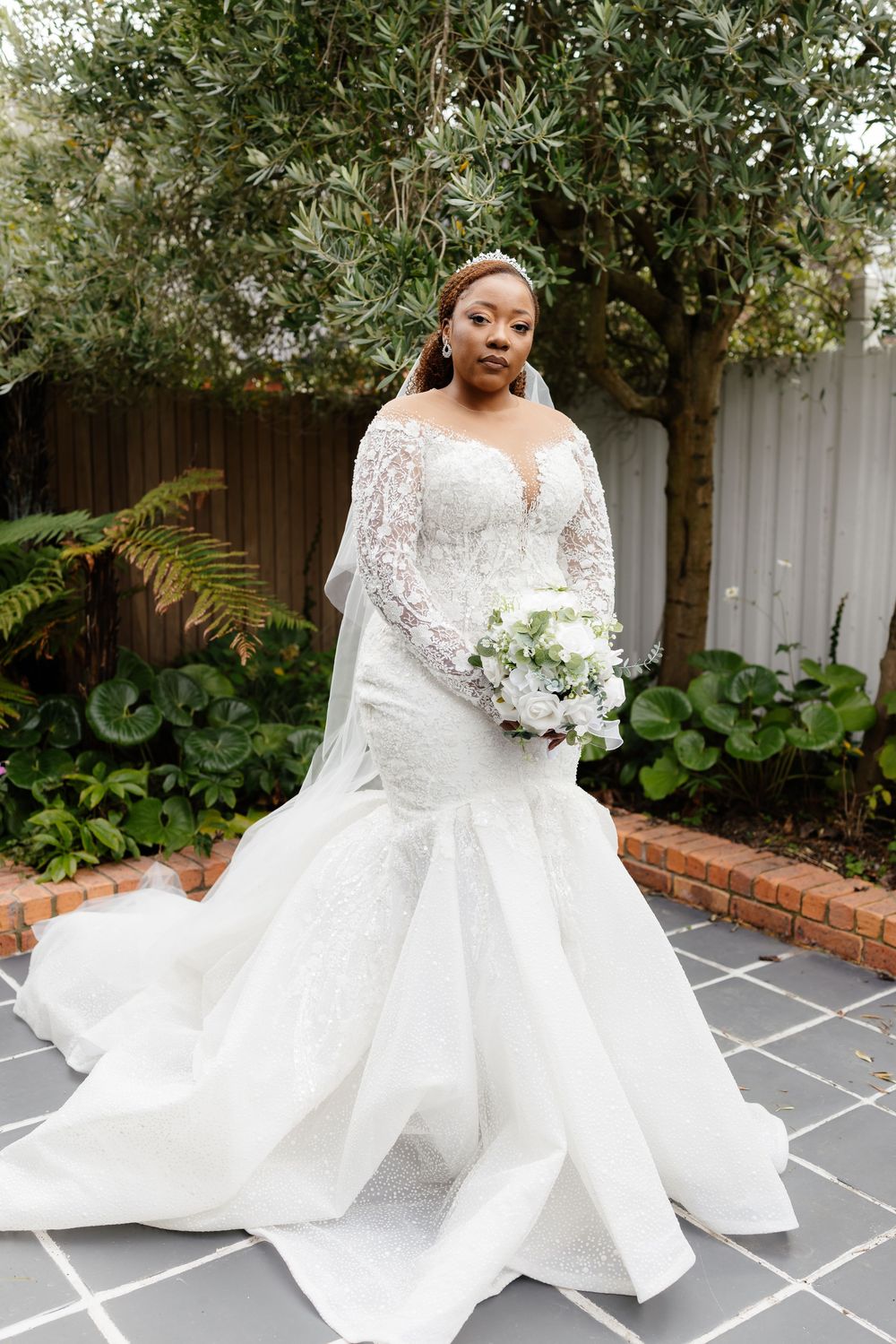 Bride in flowing white lace gown with long train twirling outdoors on stone patio.