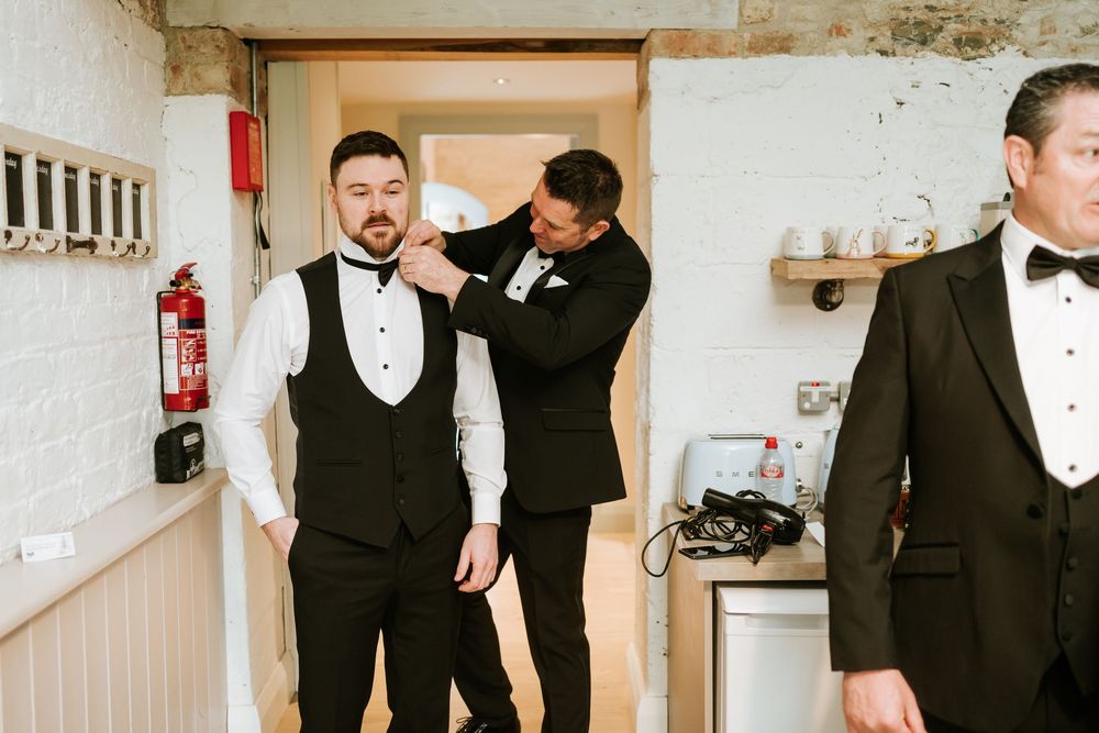 Groomsmen in black tuxedos and bowties share laughter and smiles while getting ready for a wedding celebration. Bellingham Castle