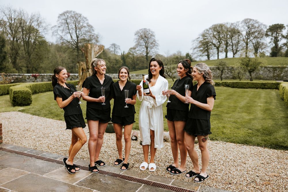 Bridesmaids in black dresses pose playfully outdoors on gravel path. Bellingham Castle Conlon Photo & Film