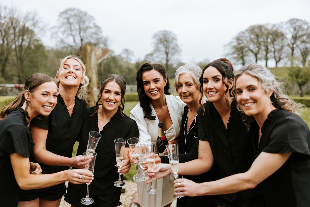 A group of wedding guests in black dresses toasting with champagne glasses in garden setting. Bellingham Castle Conlon Photo & Film
