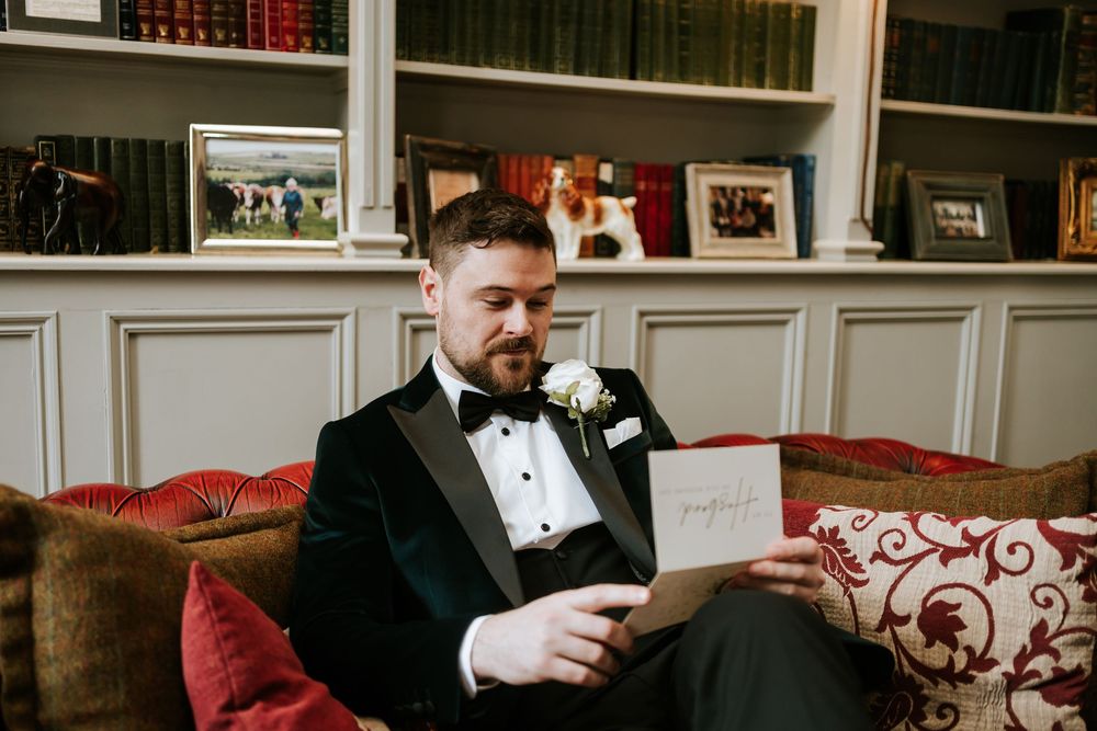 Groom and groomsmen relax on red velvet couch in formal library setting. Bellingham Castle Conlon Photo & Film