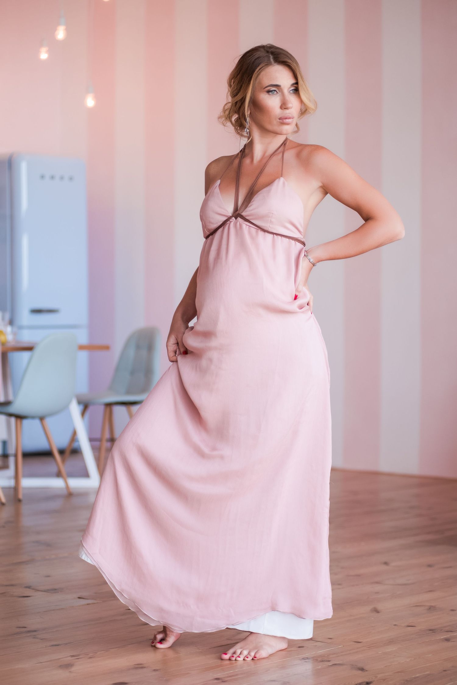 Woman in flowing pink dress twirls gracefully on wooden floor in bright interior space with white walls.