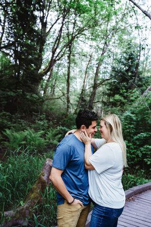 Couple sharing romantic moments on wooden walkway surrounded by lush greenery.