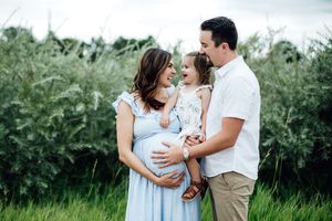 Family of three sharing joyful moments together in an outdoor field setting.