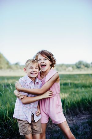 Two children laughing and hugging while playing in a grassy field.