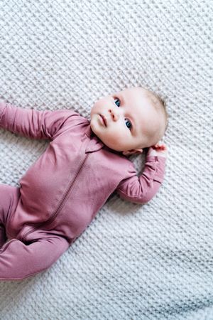 Baby in pink onesie lying on white textured blanket in progression of poses.