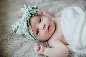 A baby wearing a mint green bow headband lies peacefully on white fabric.