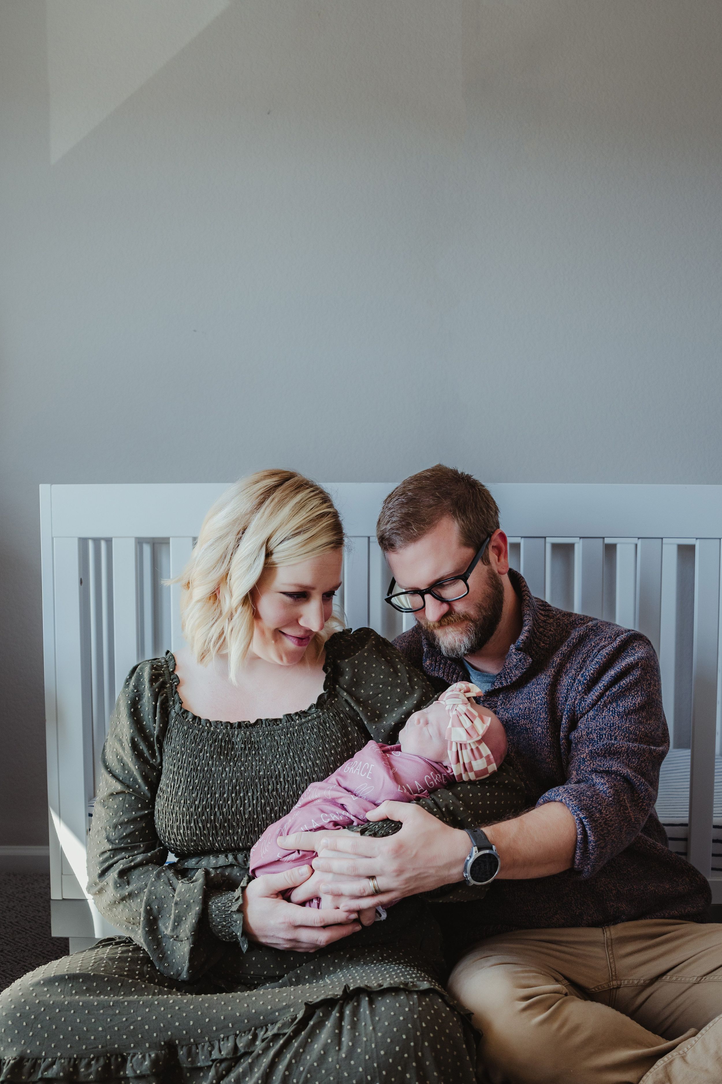 Couple snuggling with newborn baby on couch in series of intimate indoor portraits.