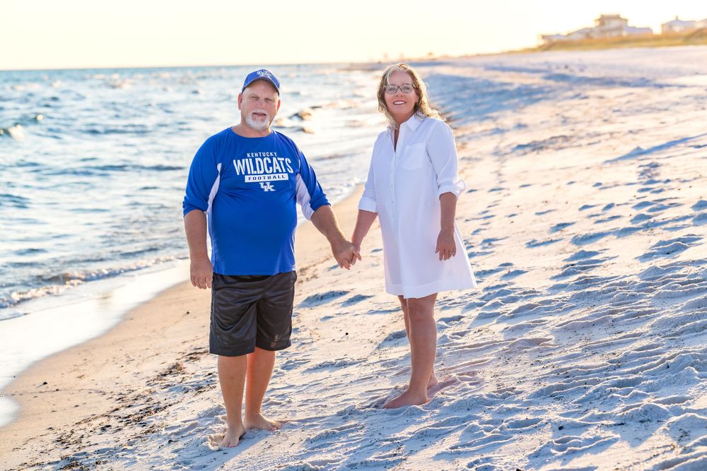 Two people walking along a sandy beach at sunset with waves gently rolling onto the shore.