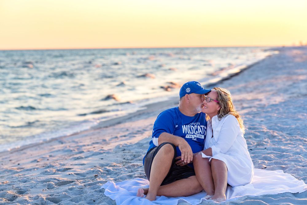 Romantic couple embraces on sandy beach at sunset with waves crashing in background.