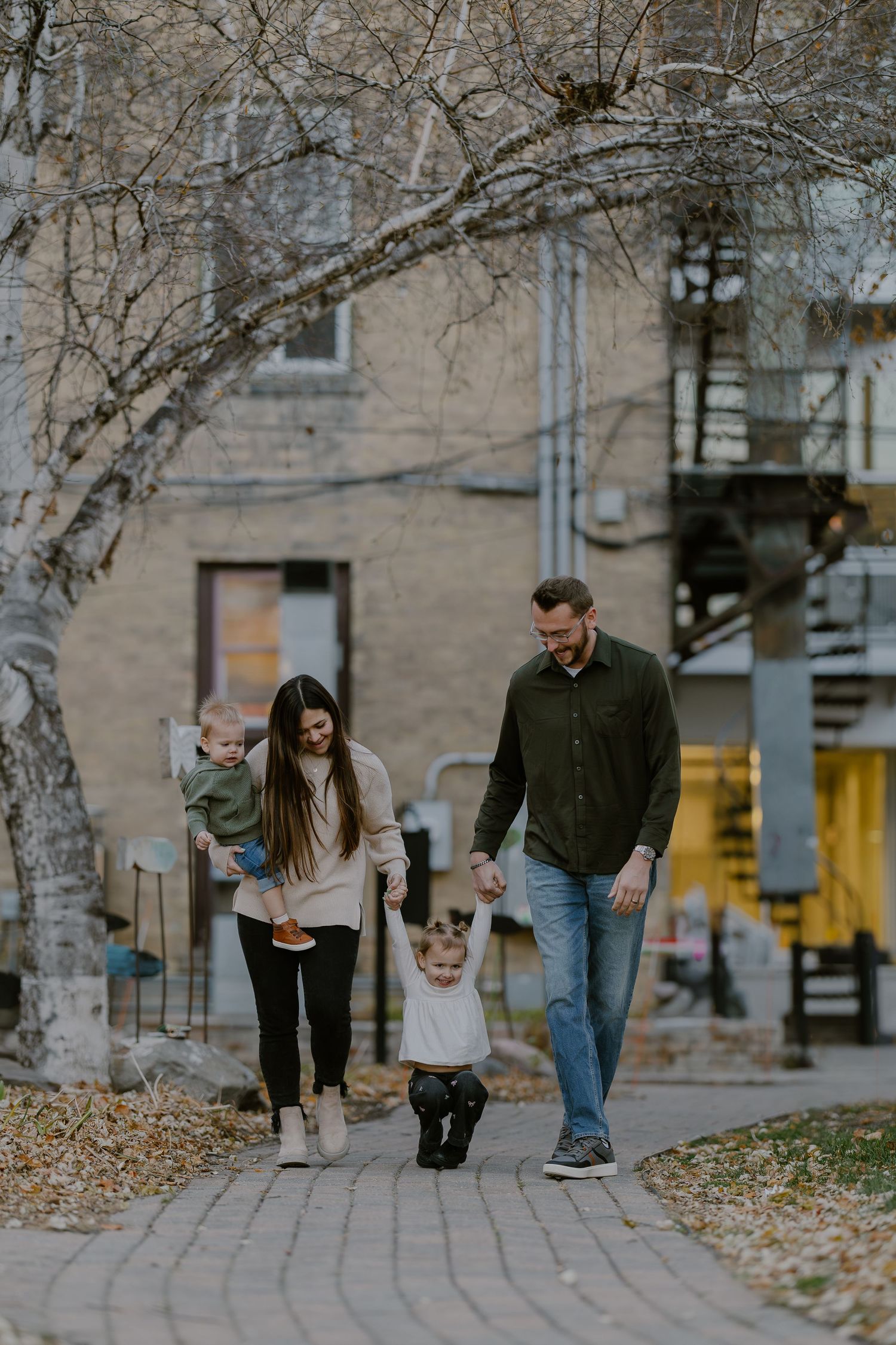 A couple walking together on a sidewalk with fallen autumn leaves and birch trees in an urban setting.