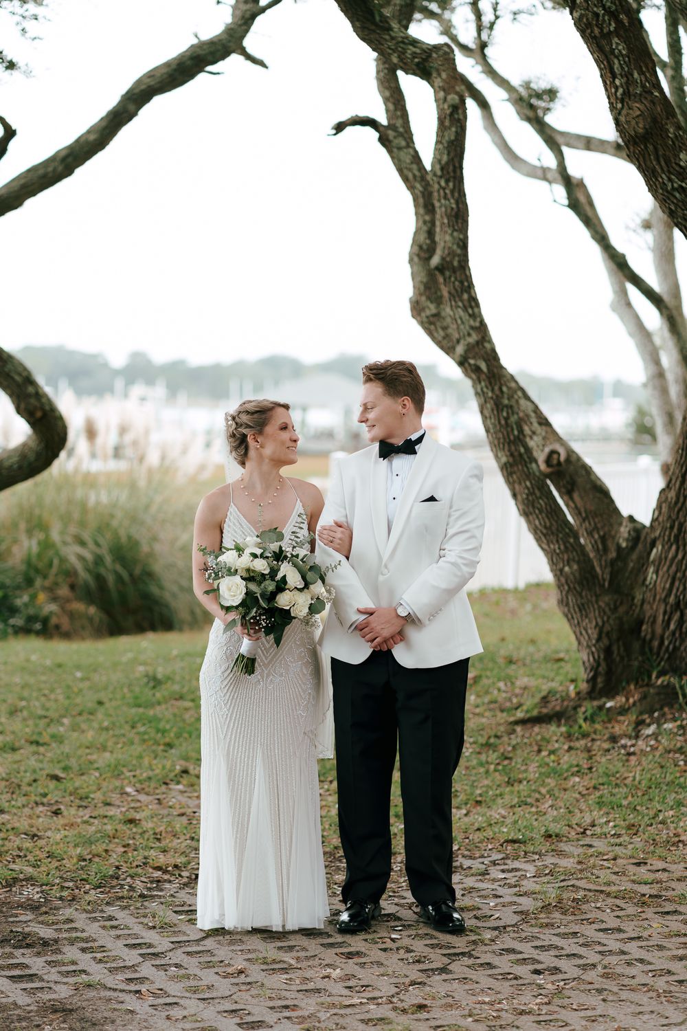 A wedding couple shares romantic moments under twisted trees along a waterfront path. Morehead City, NC