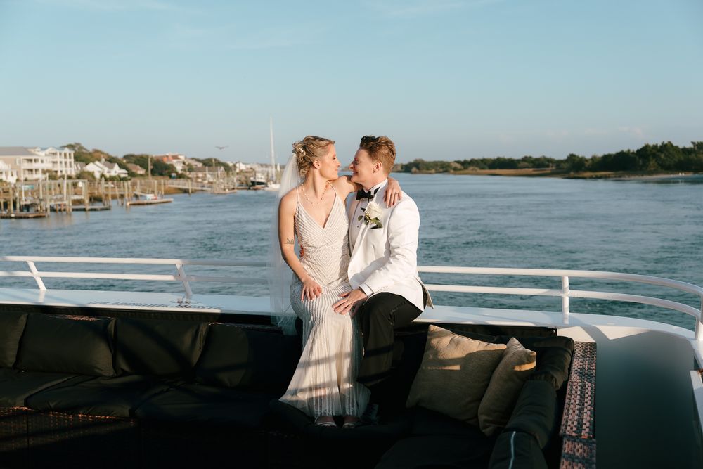 A couple shares an intimate moment on a boat deck with water and coastal homes in the background.