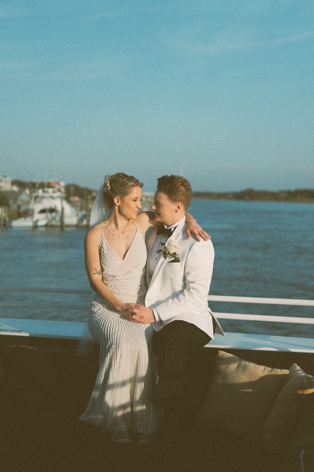 A romantic couple shares an intimate moment on a boat deck against a serene blue ocean backdrop.