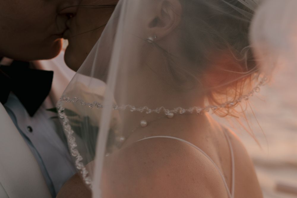A couple embraces during a romantic sunset beach wedding ceremony.