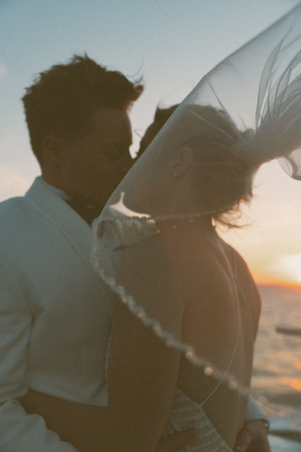 A silhouetted couple shares an intimate moment against a soft sunset sky.