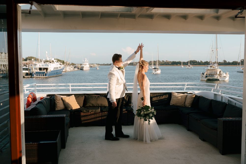 A couple celebrates their wedding day dancing together on a boat deck with a marina view behind them.