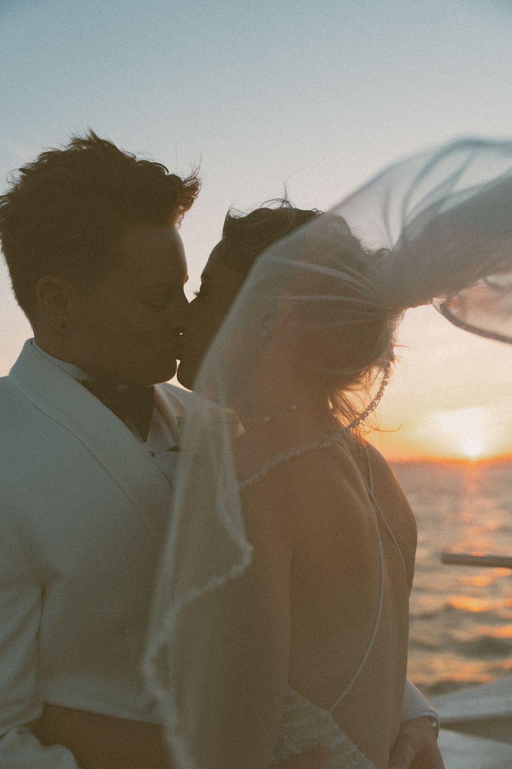 Silhouetted couple embraces against a golden sunset over ocean waters.