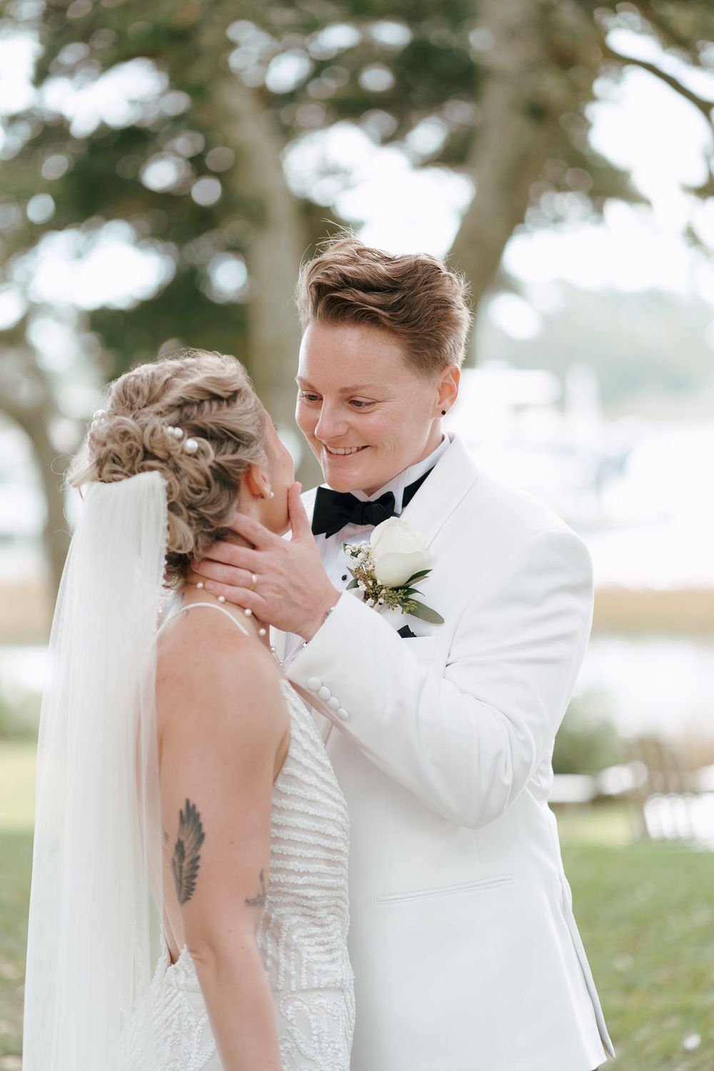 A romantic first look moment between newlyweds outdoors with the groom in a white tuxedo jacket and bride in white dress.