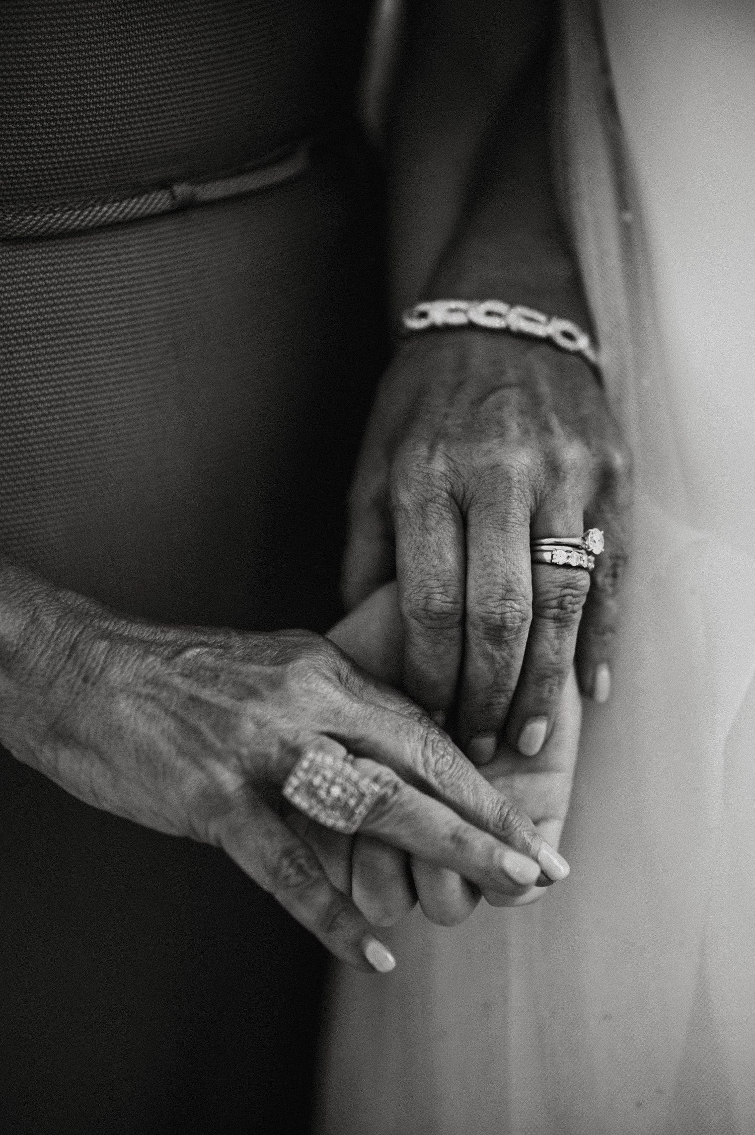 A black and white close-up of hands wearing elegant rings and bracelets, showing intricate jewelry details.