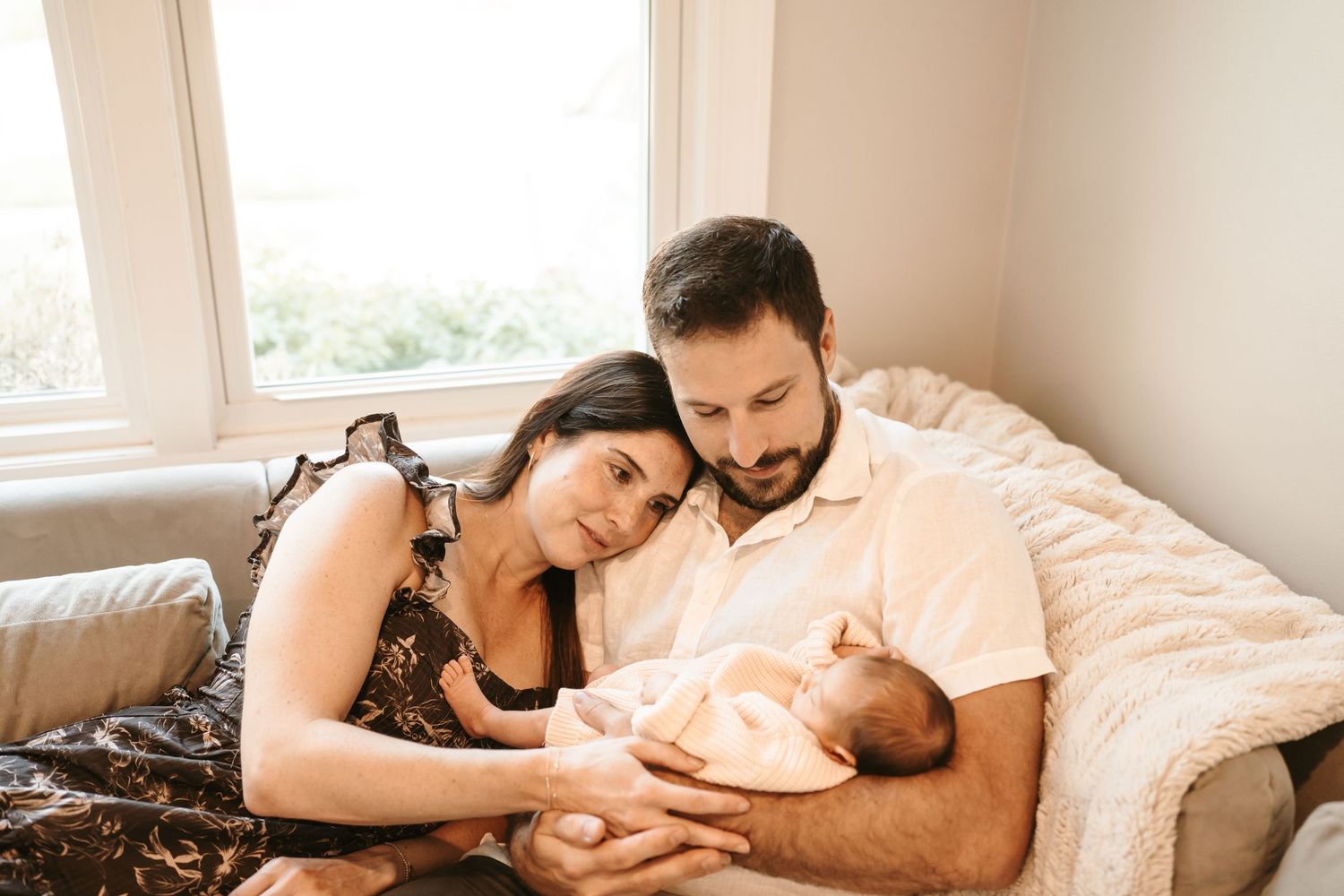 Parents and baby lying together on bed in natural light, sharing tender moments in series of intimate family photos.