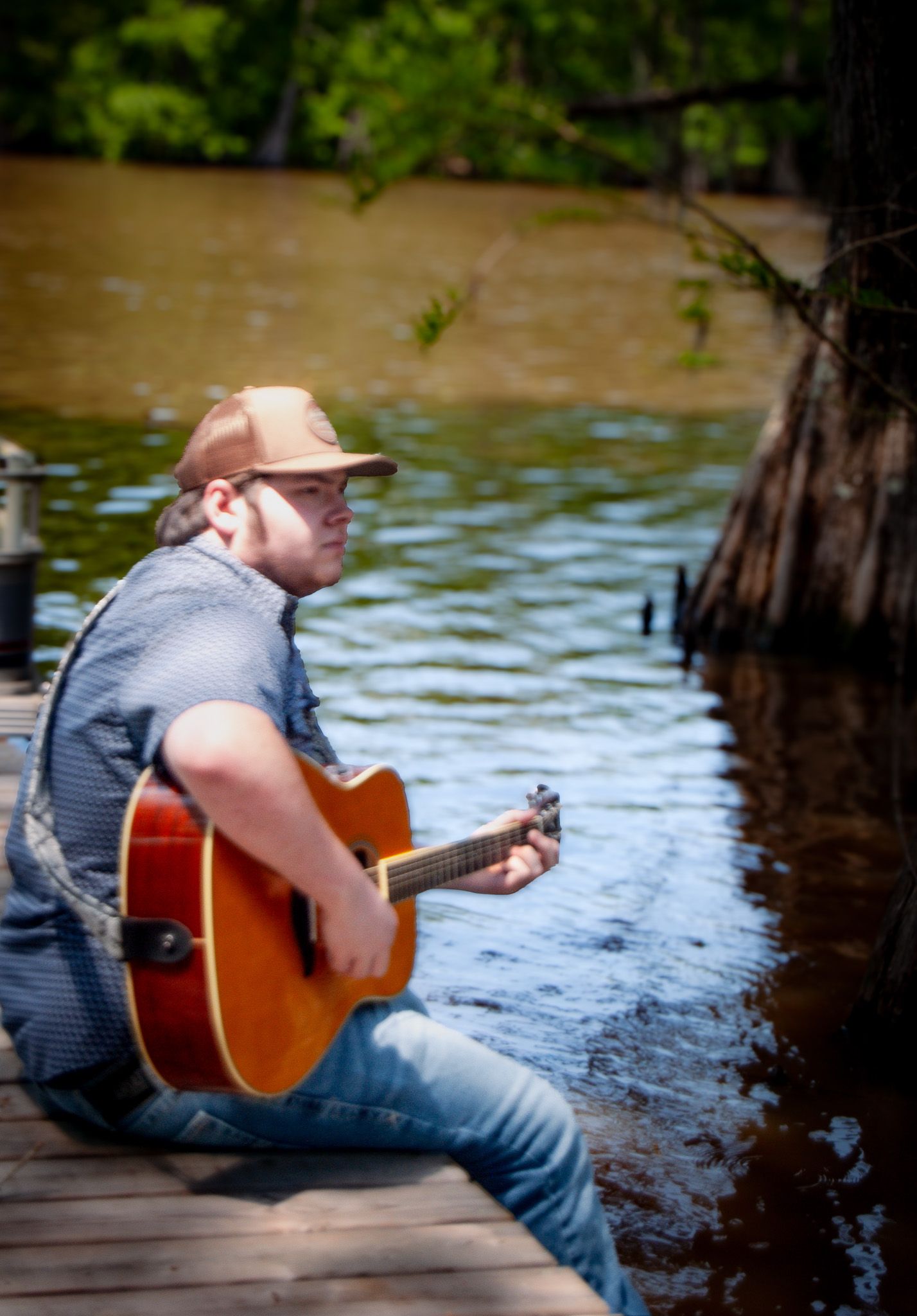 Side view of musician playing guitar on wooden dock over water.