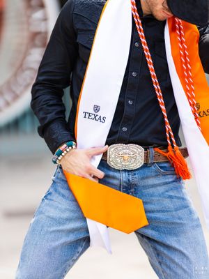 Detail shot of graduation stole and belt buckle with Texas university branding.