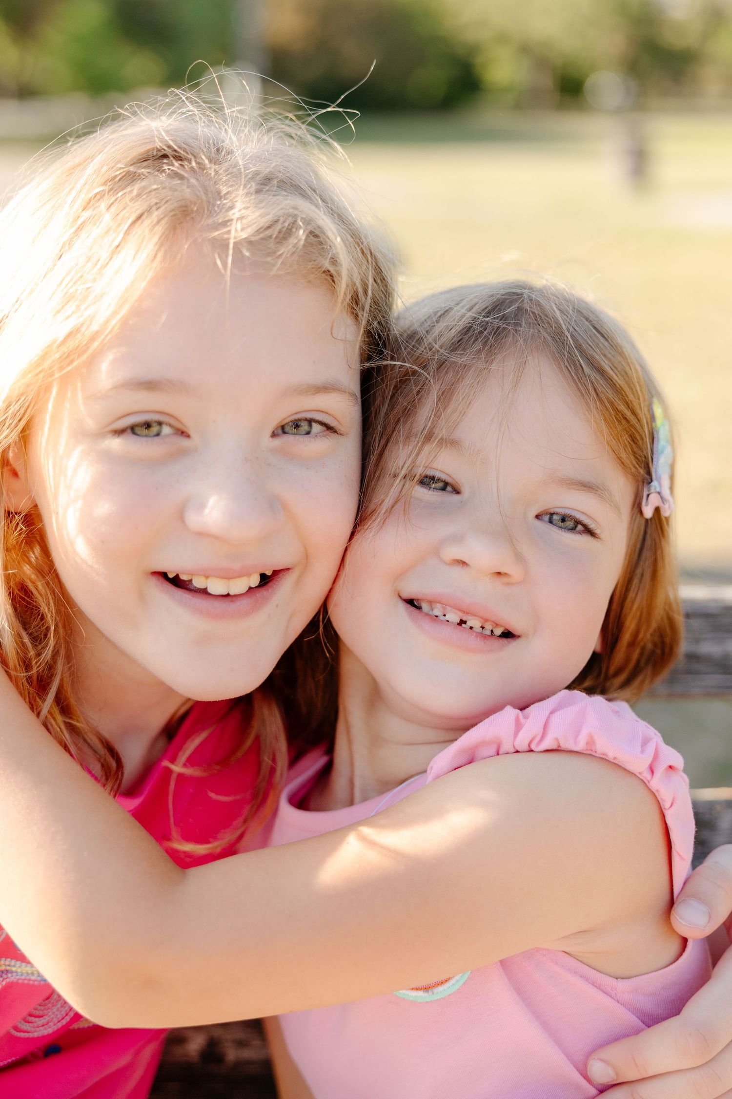 Two smiling children embrace and share a joyful moment together in bright outdoor lighting.