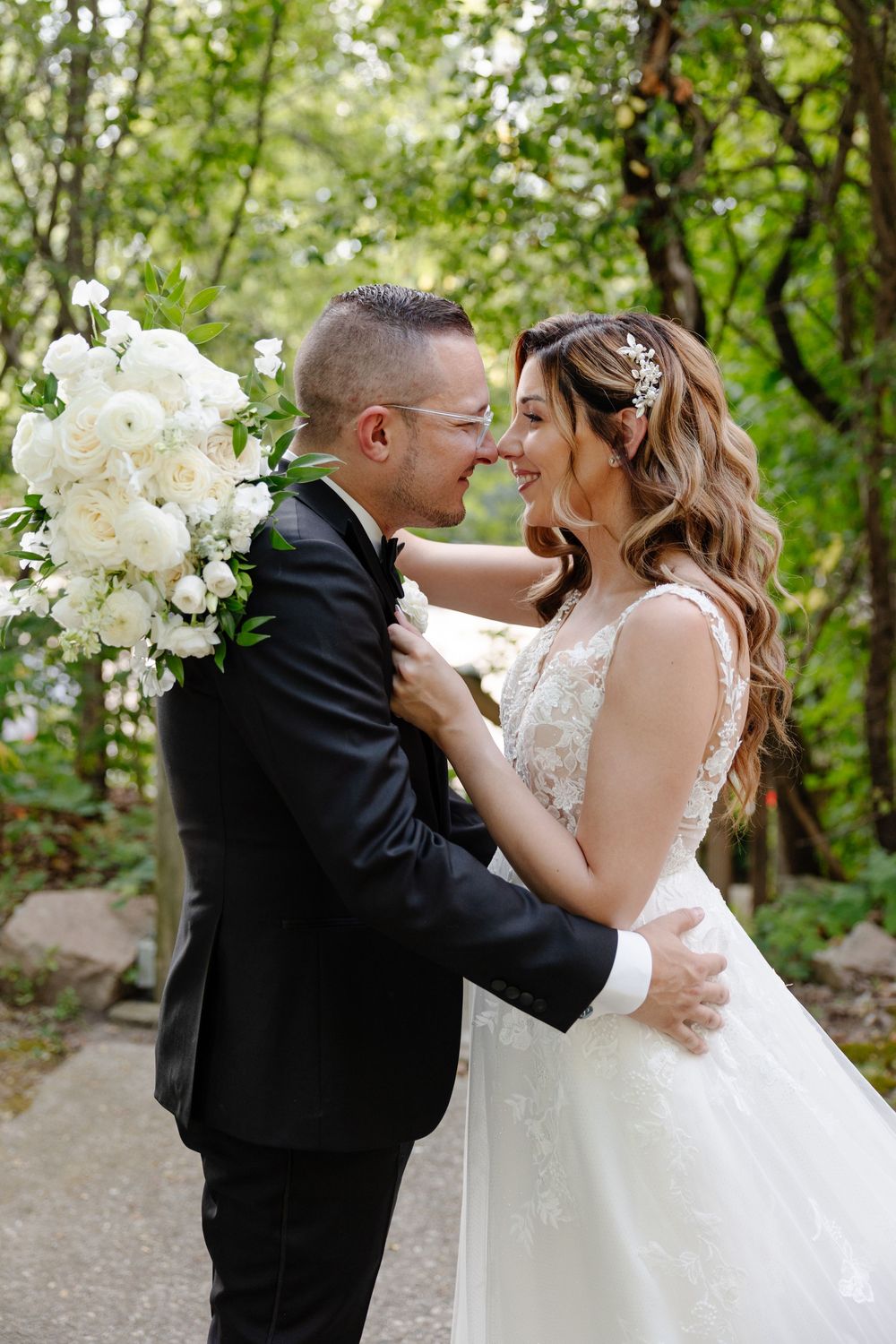 A romantic wedding moment captured in a lush garden setting with white floral decorations and natural greenery.
