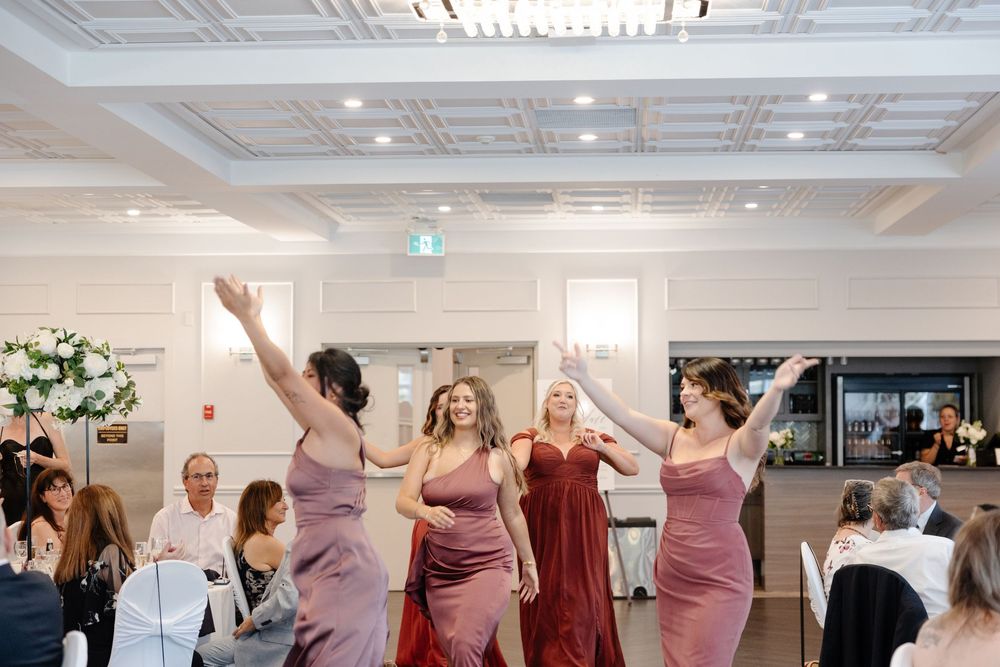 Wedding guests dancing and celebrating together at a reception in an elegant ballroom with white decor.