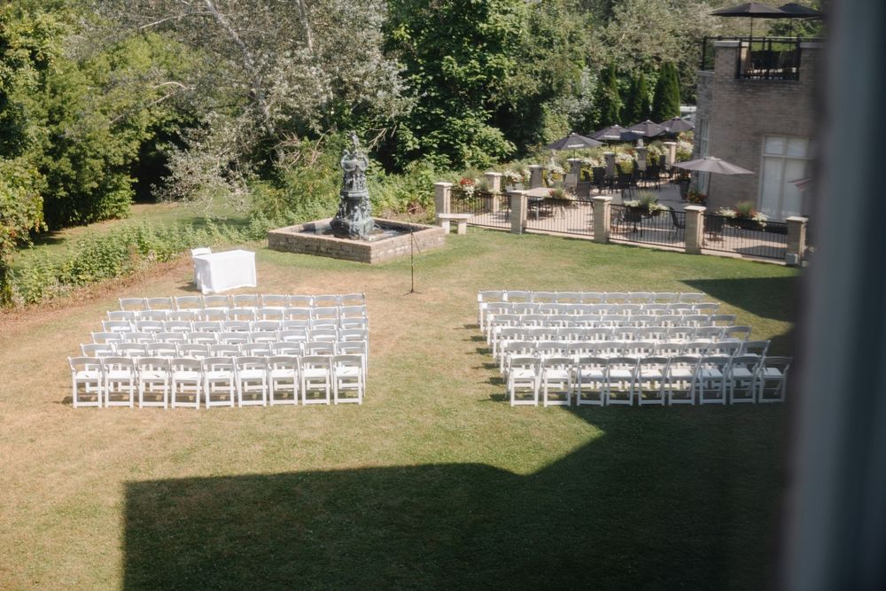 White chairs arranged in rows on a grassy lawn for an outdoor wedding ceremony with a stone structure in the background.