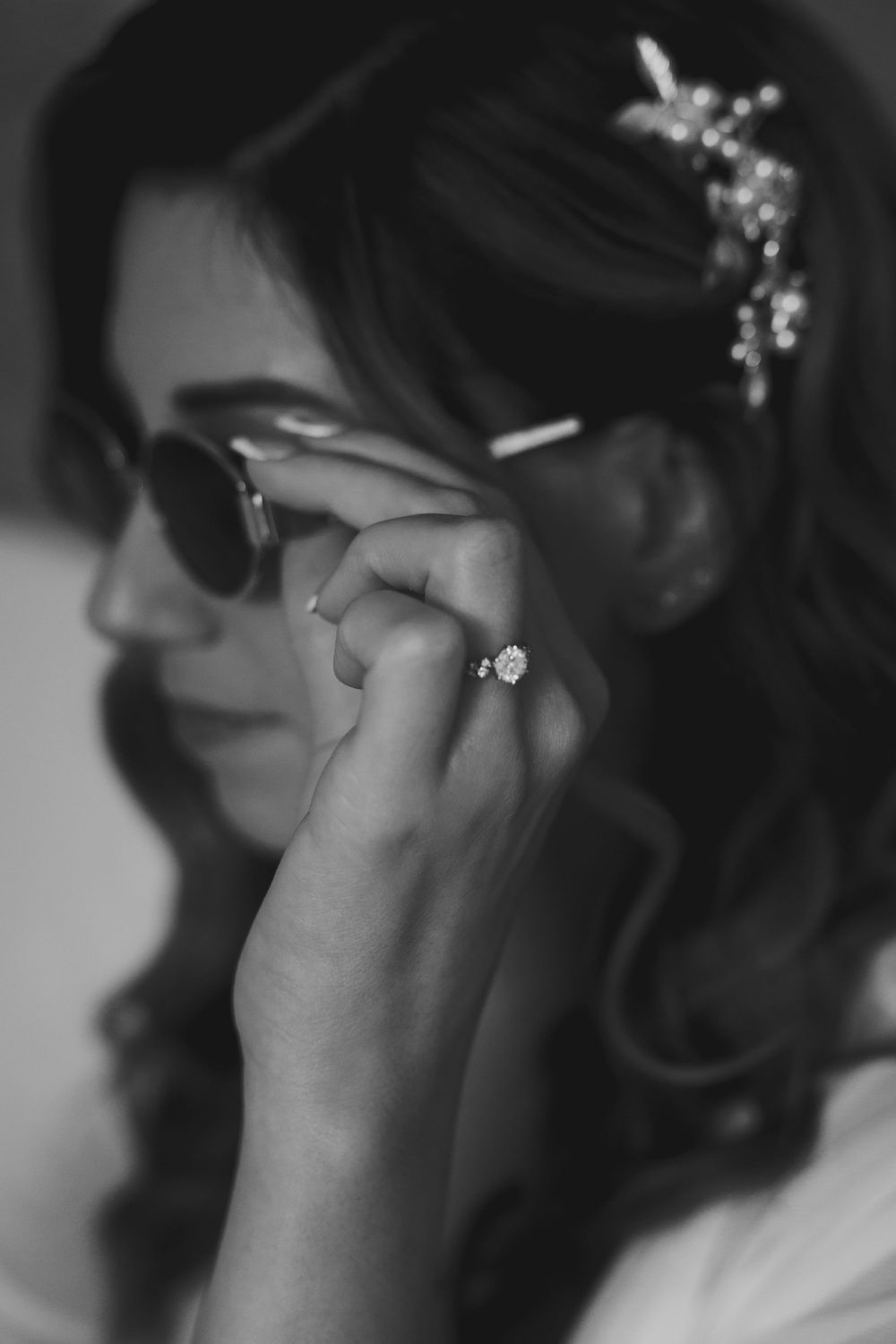 Black and white close-up of someone wearing earrings and having their makeup applied during a wedding preparation.