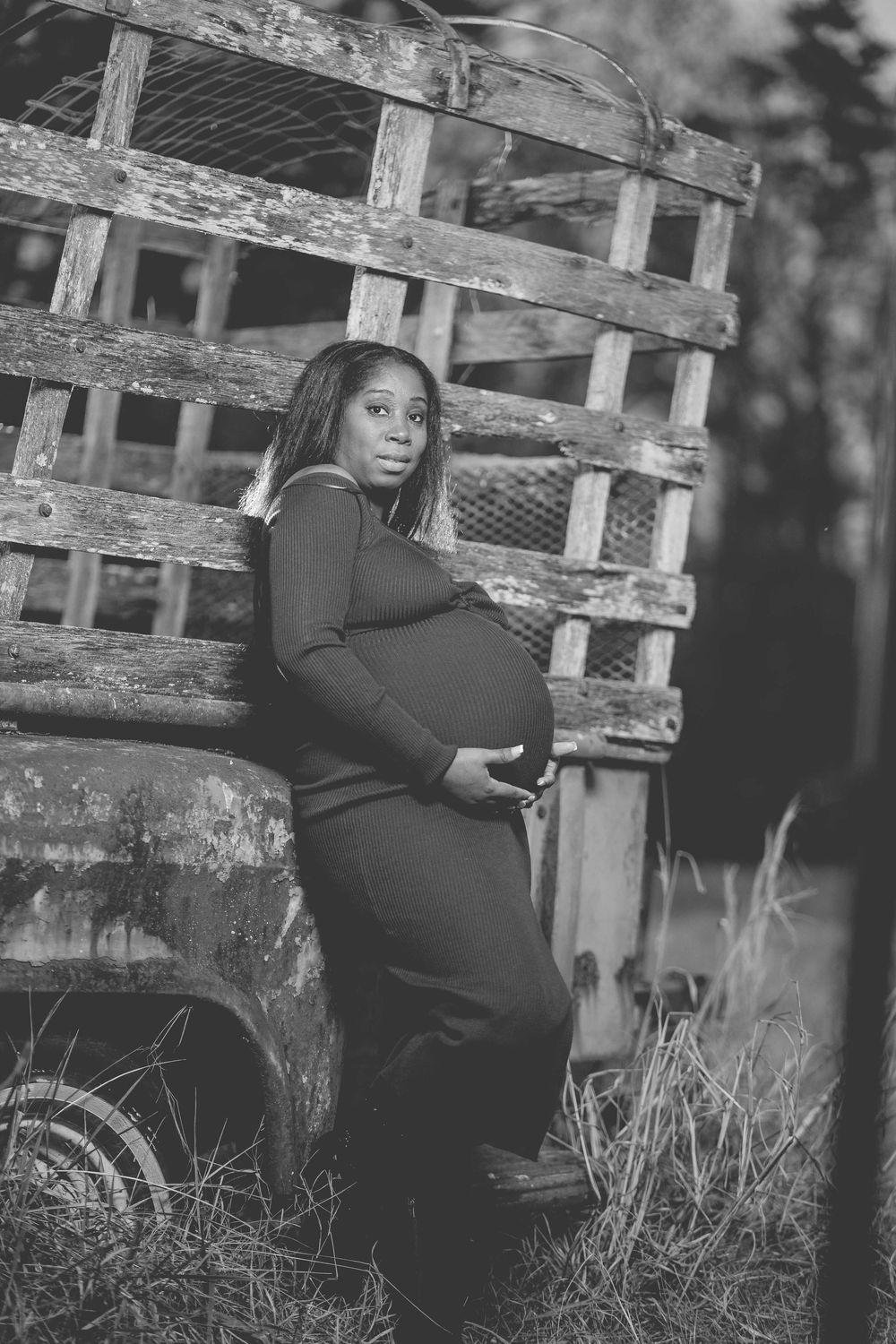 A person in a black dress poses against a rustic wooden fence in a series of black and white portraits. Maternity Session @ Stone Crest