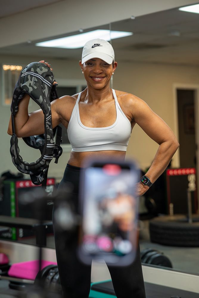 Athletic person in white Nike cap and sports bra poses with fitness equipment in a gym setting.