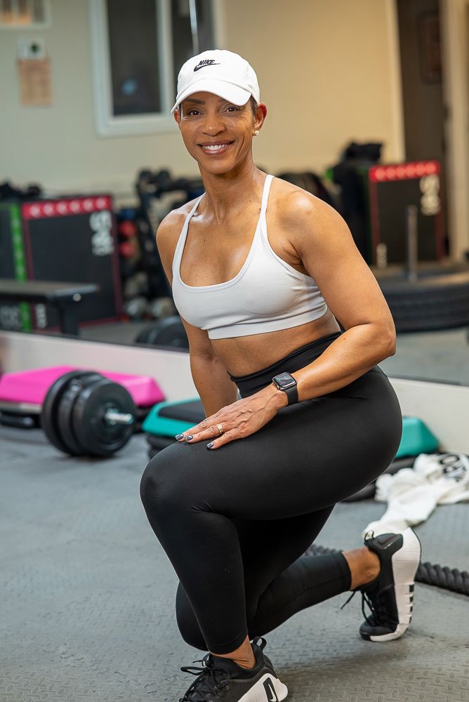 Athletic person in white tank top and black leggings performs squats during workout at gym.