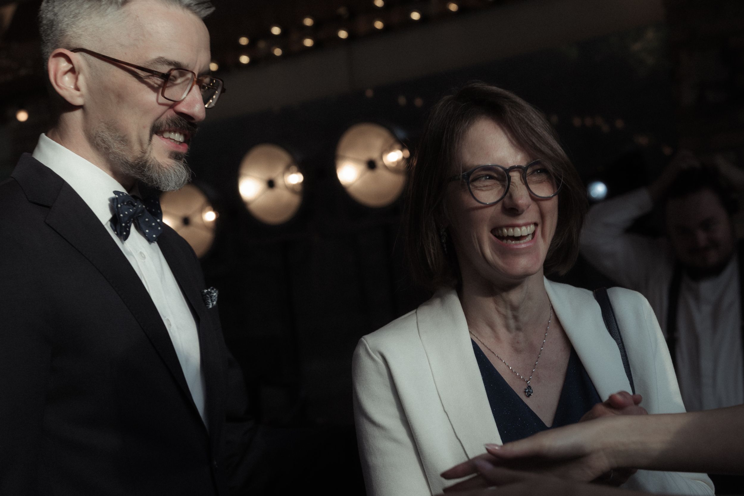 People in formal attire enjoying conversation at an evening event with ambient lighting.