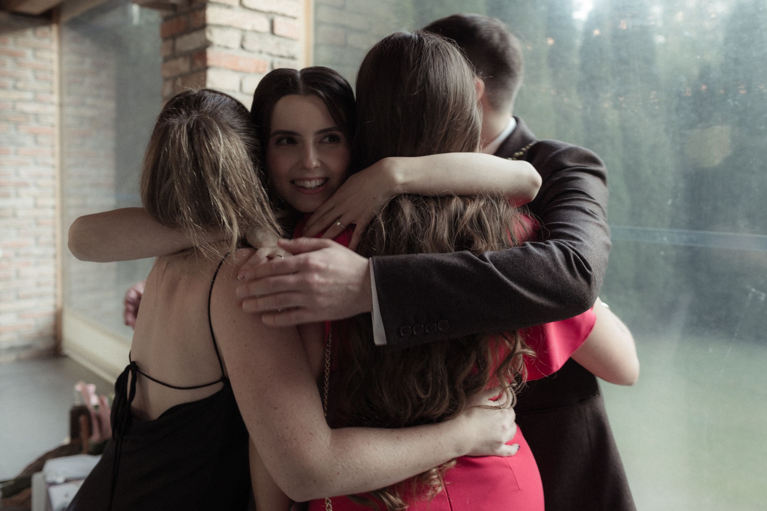 People embracing in an emotional moment near a brick wall and window.