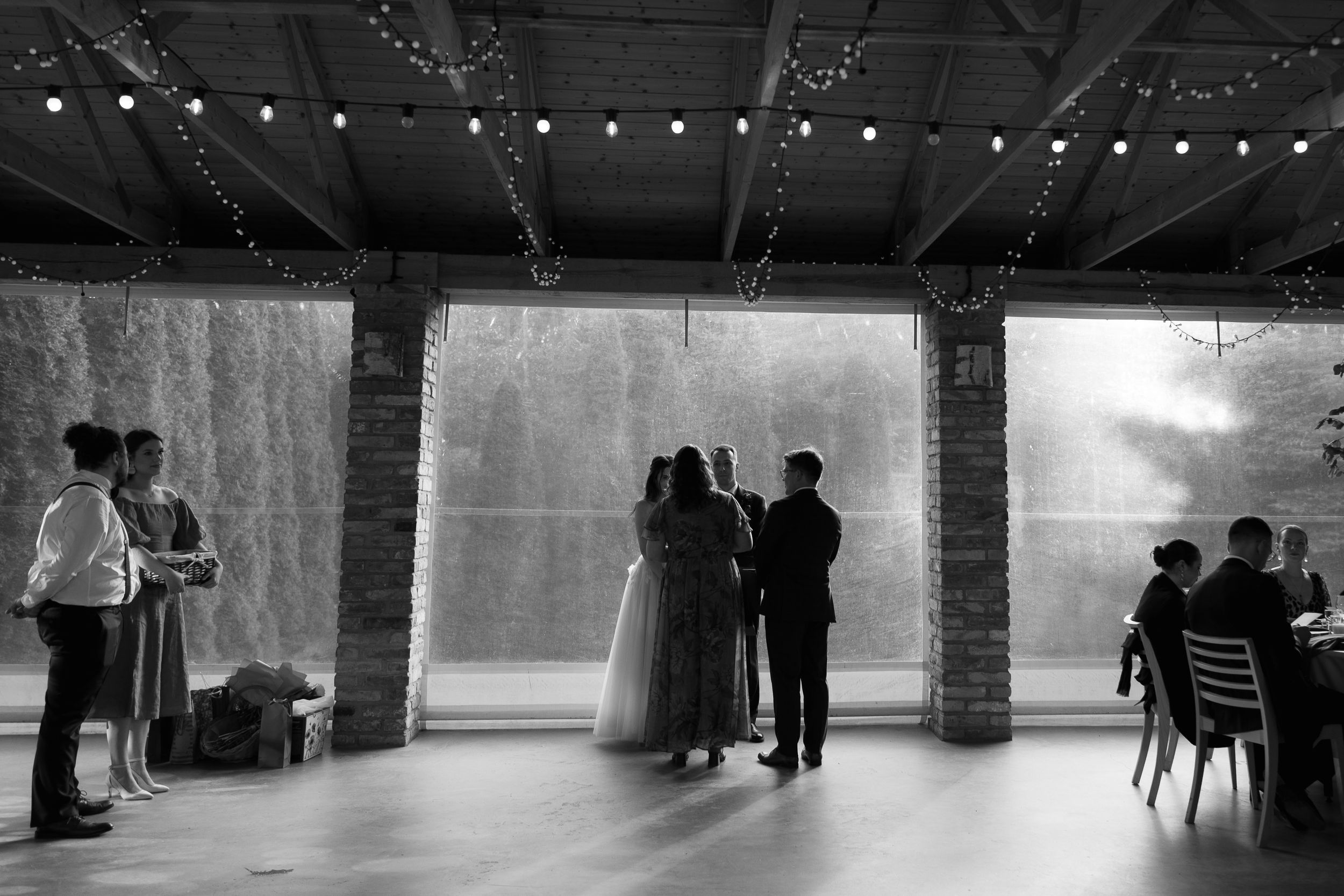 A black and white wedding reception photo showing silhouettes of guests and a couple standing under an illuminated archway.