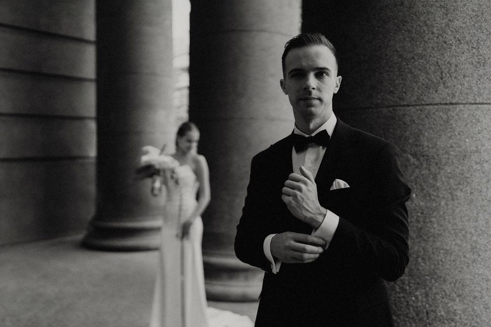 Wedding couple stands among dramatic stone pillars in black and white photography.