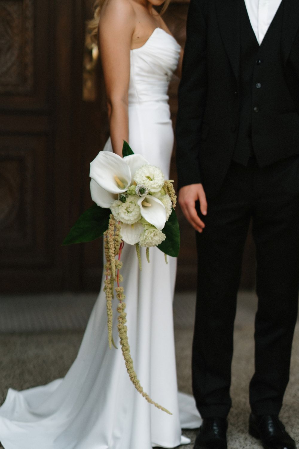 Bride in white gown holds cascading bouquet next to groom in classic tuxedo.