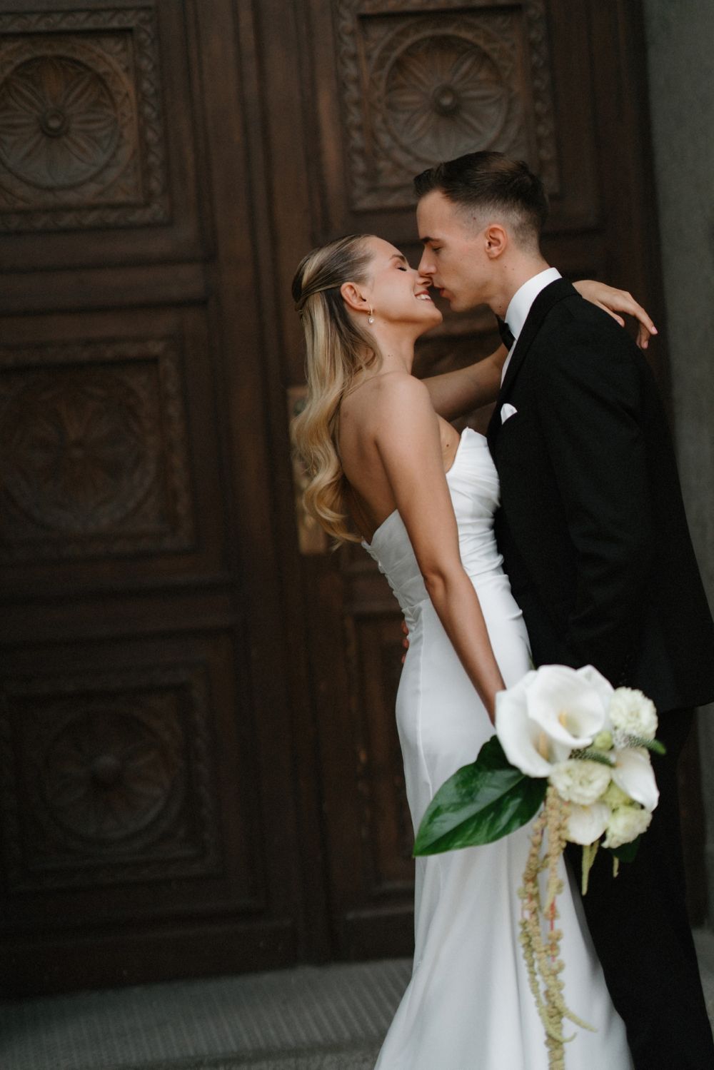 Romantic wedding moment captured between stone columns with ornate wooden doors.
