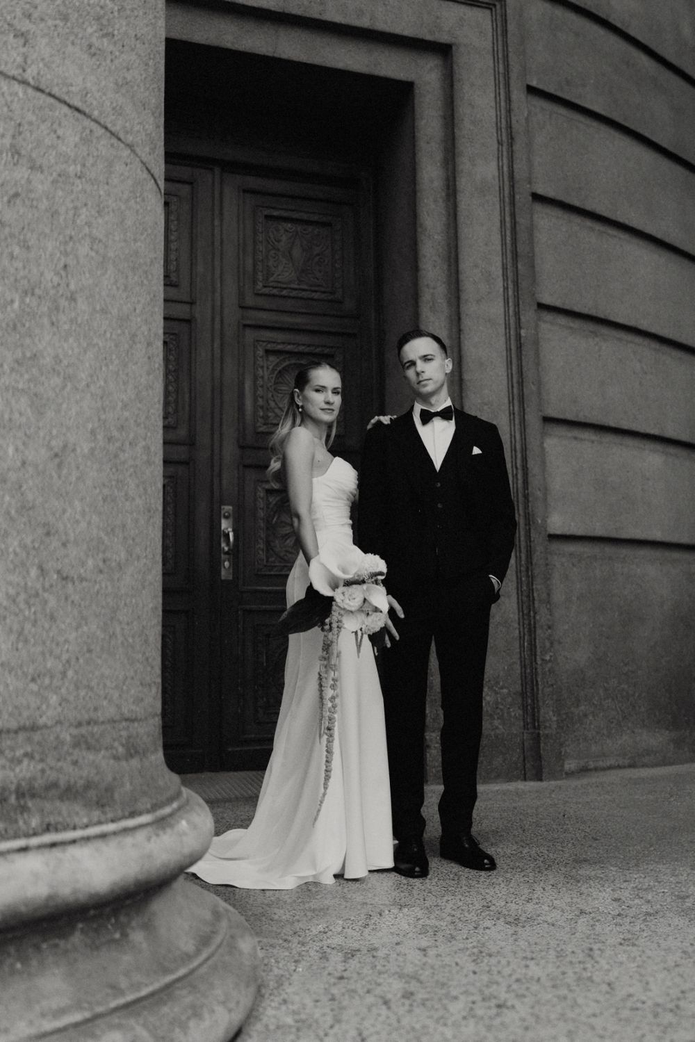 Black and white wedding portrait showcasing elegant couple against stone architecture.