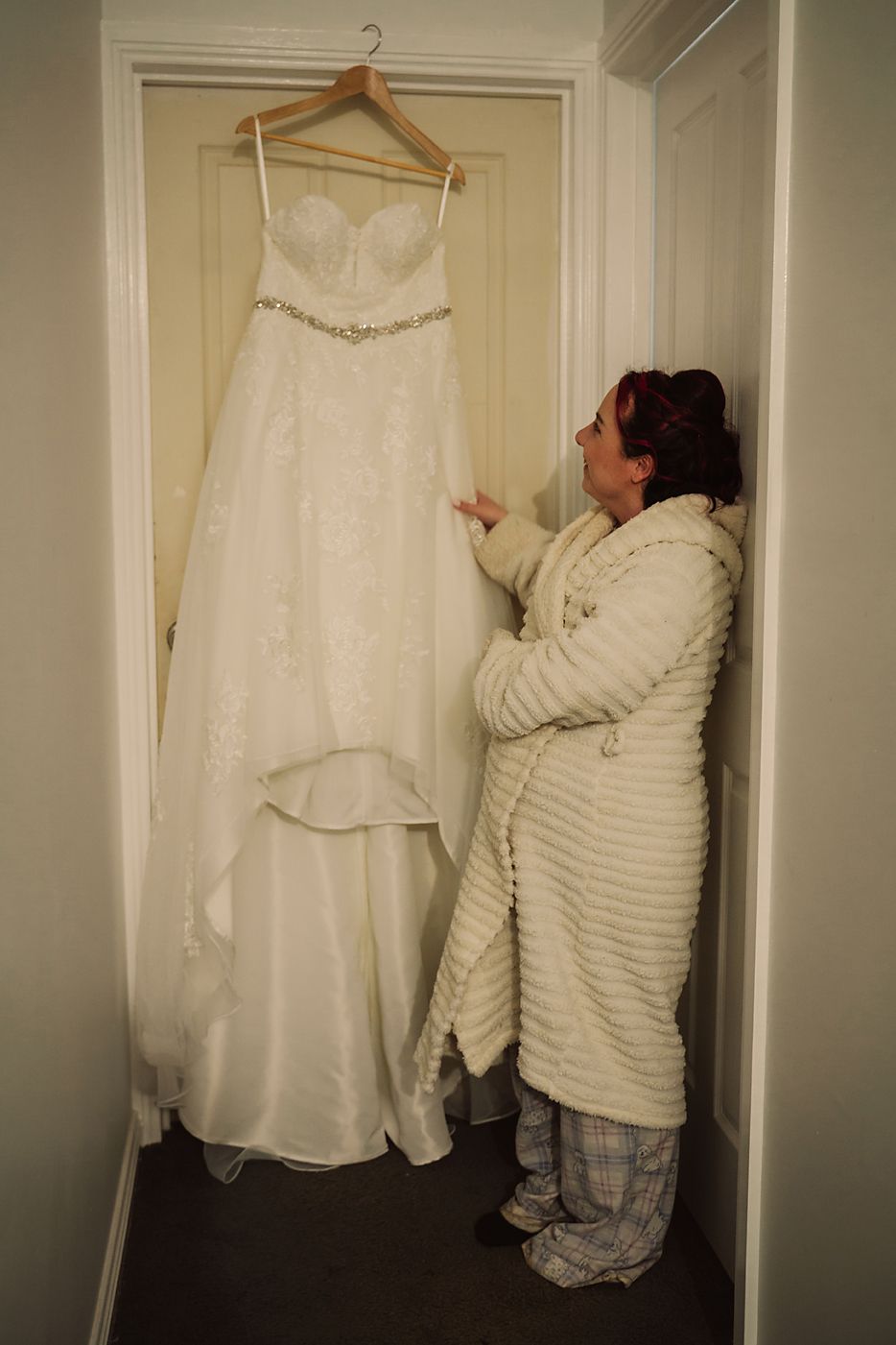 A sequence of photos showing a person hanging up a white wedding dress on a hanger against a white wall.