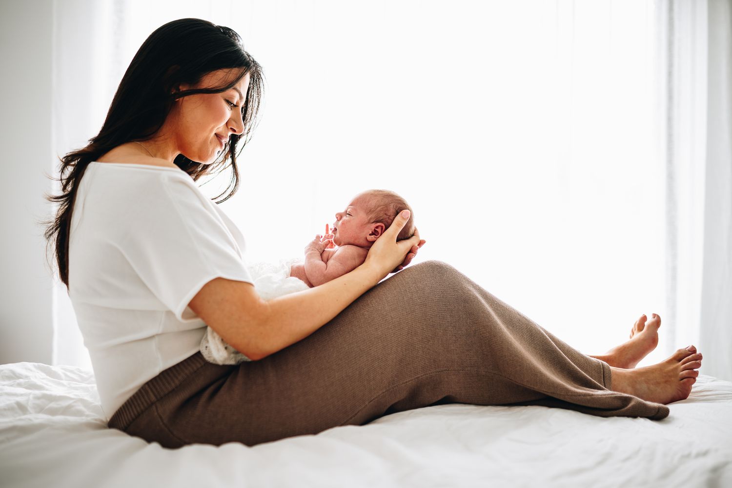 Tender moments between mom and newborn baby shown in soft, natural light against white bedding taken by a Melbourne newborn photographer.
