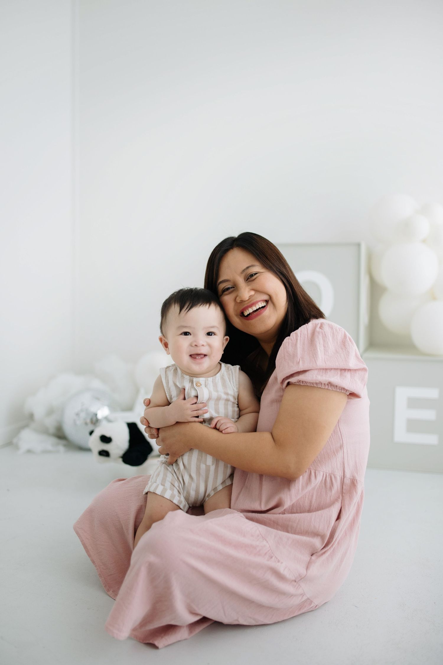 Parent and child share joyful moments together on white bedding while wearing pink and white outfits.