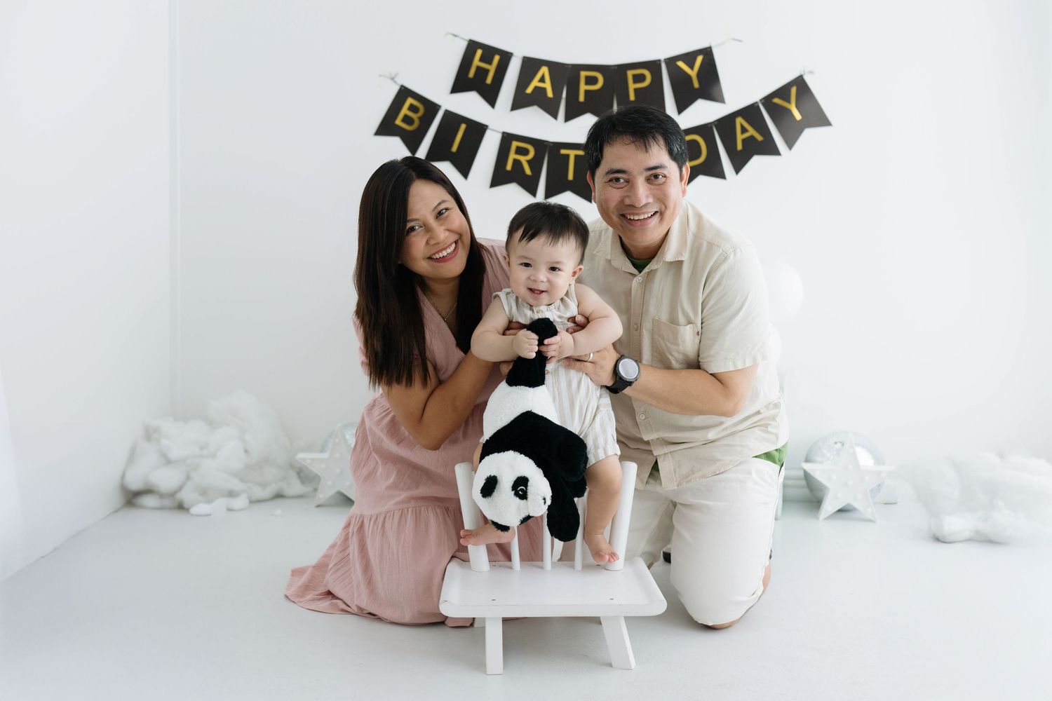 Family in matching white and pink outfits poses with their dog during a photo session against a white backdrop.